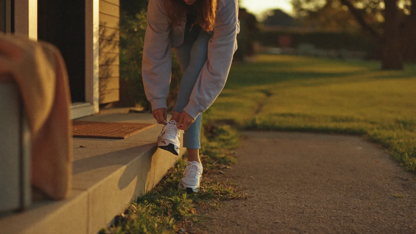 Person tying running shoes on a front doorstep at golden hour, about to take an evening walk