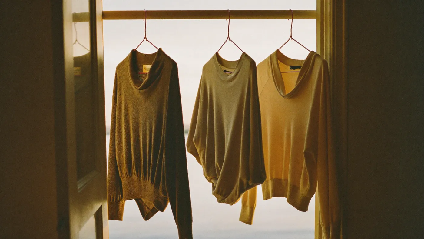 Three identical outfits hanging on an open wardrobe rail in soft morning light, simple and orderly
