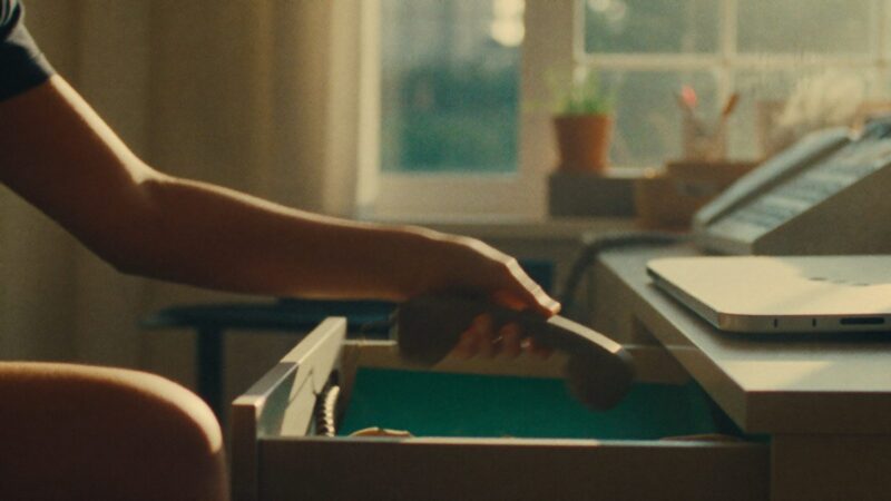 Person placing a phone face-down into a desk drawer in a bright home office, morning light, relieved exhale