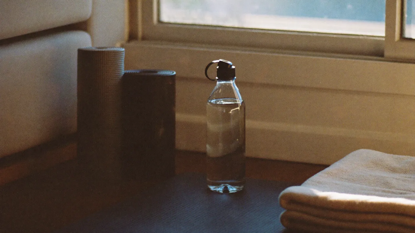A rolled yoga mat, water bottle, and folded towel beside a sunlit living-room window