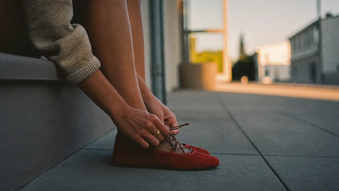 Person tying shoelaces on a doorstep at dawn, calm and ready, soft early light on a quiet street