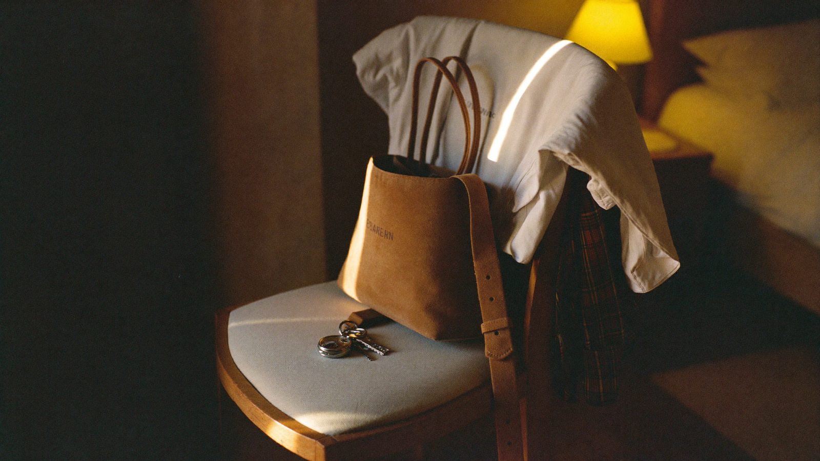 Clothes laid out neatly on a chair the night before a big day, with a watch and keys on the seat, warm bedside lamp light