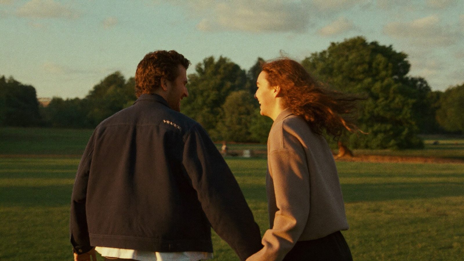 Two adults laughing while walking side by side through a park in golden light, seen from behind