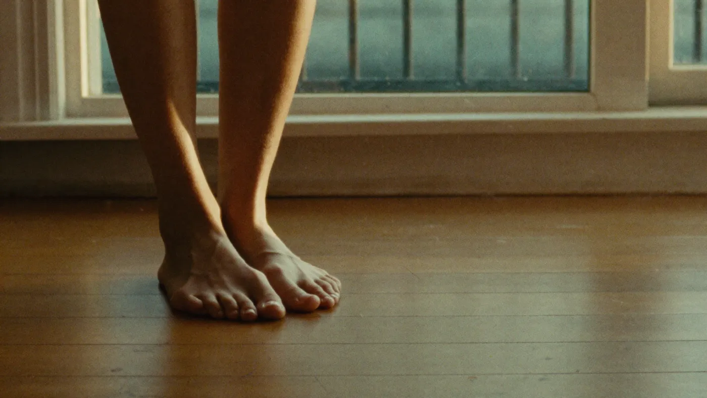 Bare feet grounded on a warm wooden floor beside a window, soft pooled light, quiet stillness