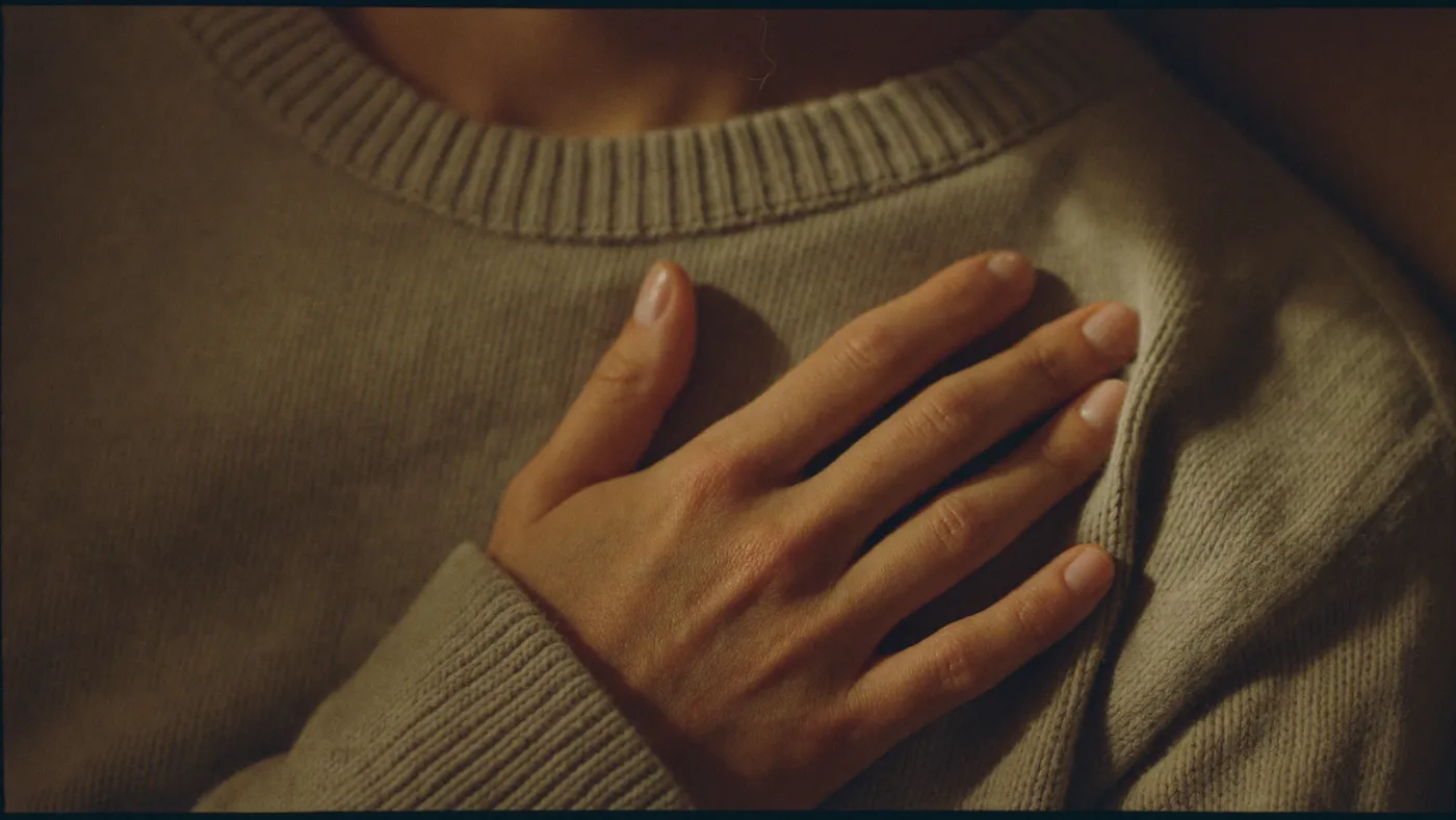 Close-up of a hand pressed gently to the chest over a soft sweater, slow calm breathing, warm indoor light