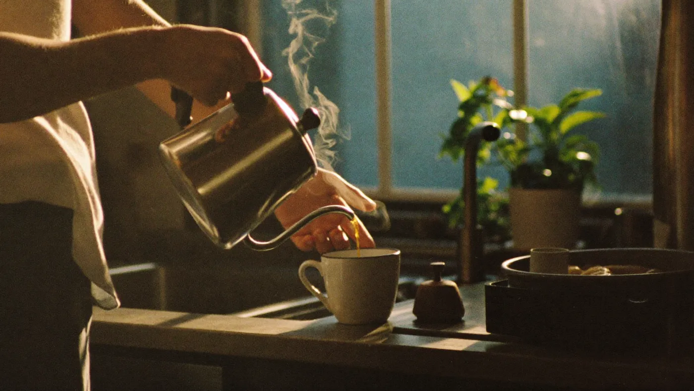 Unhurried hands making pour-over coffee in a sunlit kitchen, steam rising slowly