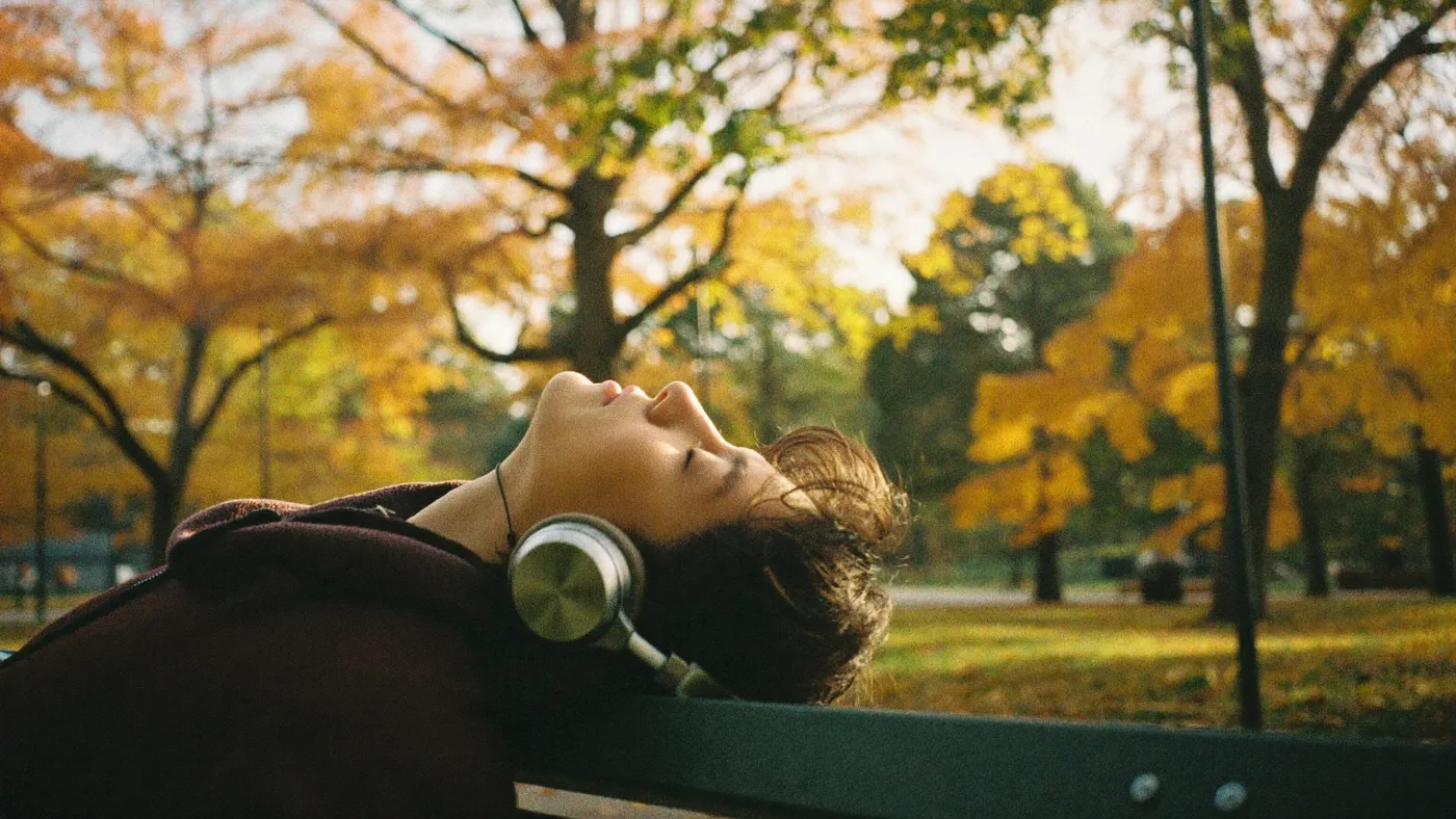 Person with over-ear headphones resting on a park bench, eyes closed, peaceful
