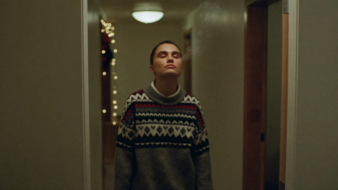 Person taking a quiet breath alone in a cozy hallway, holiday string lights softly blurred in the background