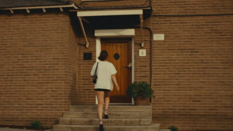Person walking up the steps of a quiet brick building entrance with glass doors in morning light, calm and resolved