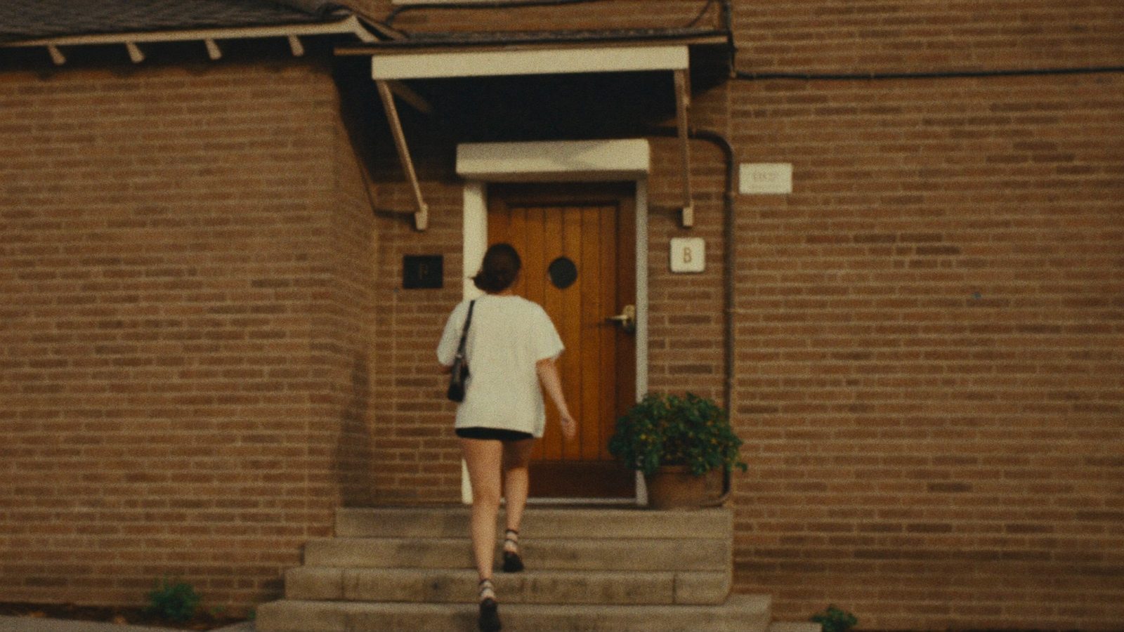 Person walking up the steps of a quiet brick building entrance with glass doors in morning light, calm and resolved