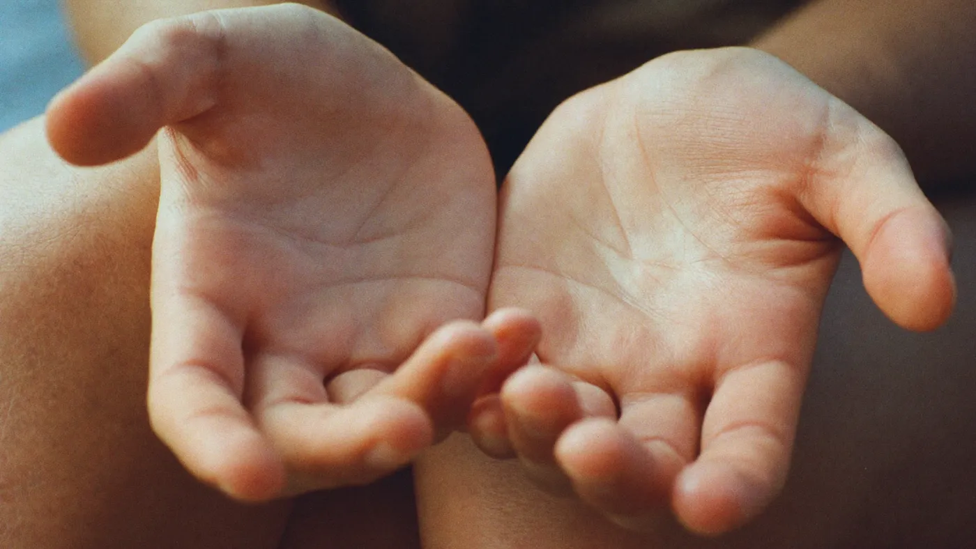 Close-up of hands slowly unclenching and resting open on knees, warm soft light, shallow focus
