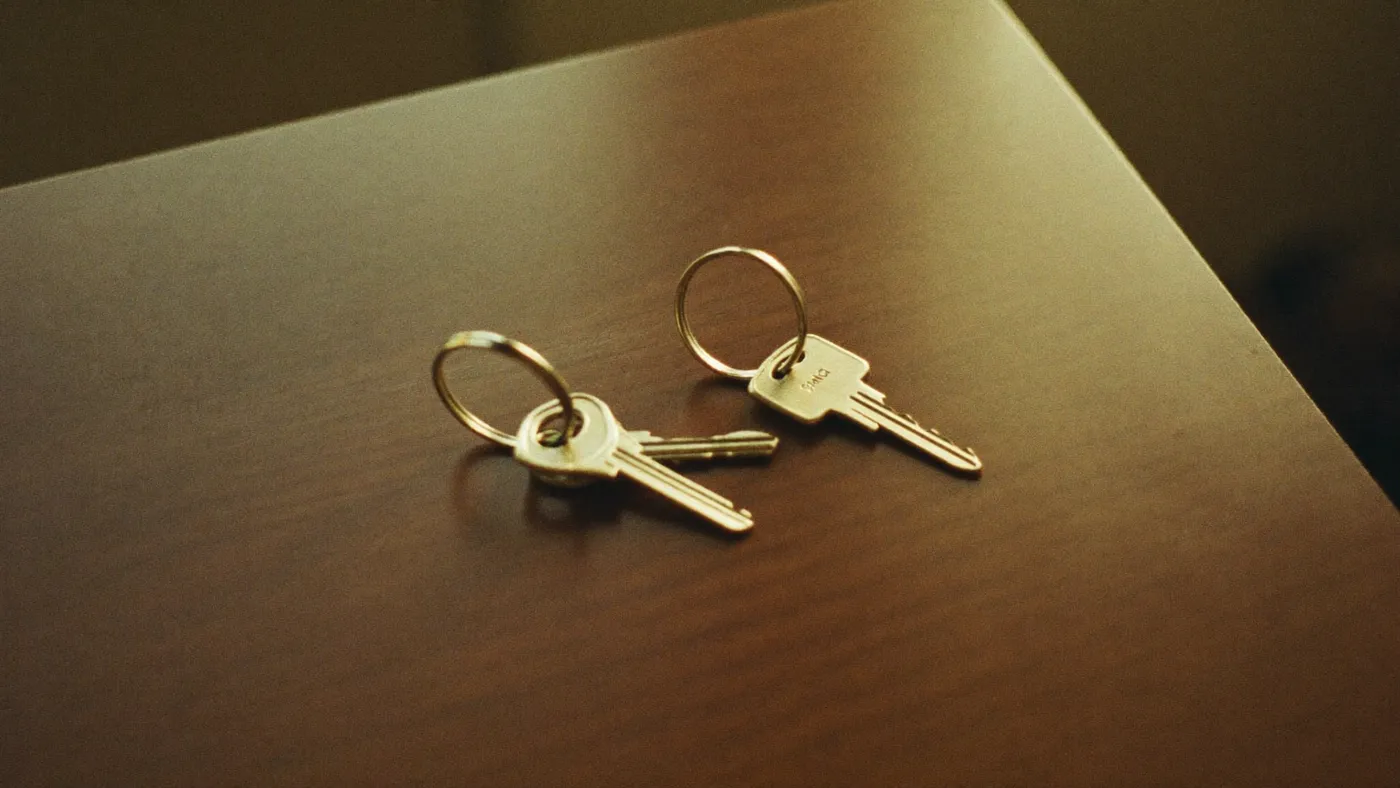 Two sets of house keys on a wooden table in morning light, one set slightly apart from the other