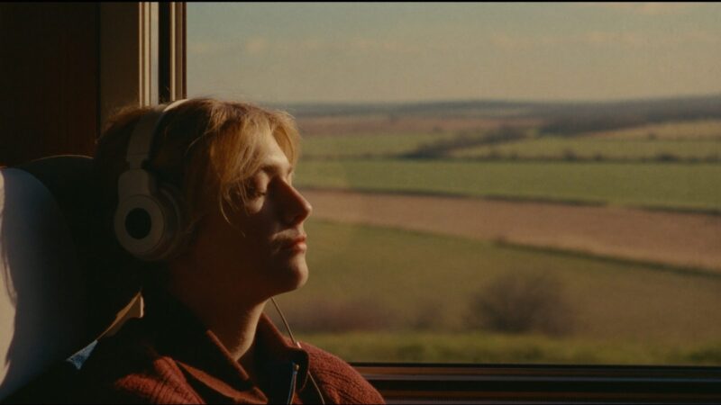 Person with over-ear headphones sitting quietly by a window on a train, soft light, peaceful