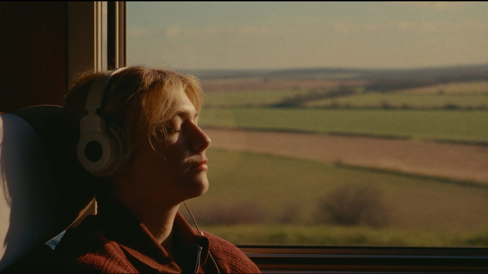 Person with over-ear headphones sitting quietly by a window on a train, soft light, peaceful