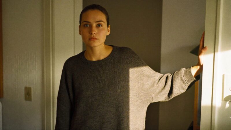 Person standing in a doorway with a hand resting on the frame, calm steady expression, soft afternoon light inside