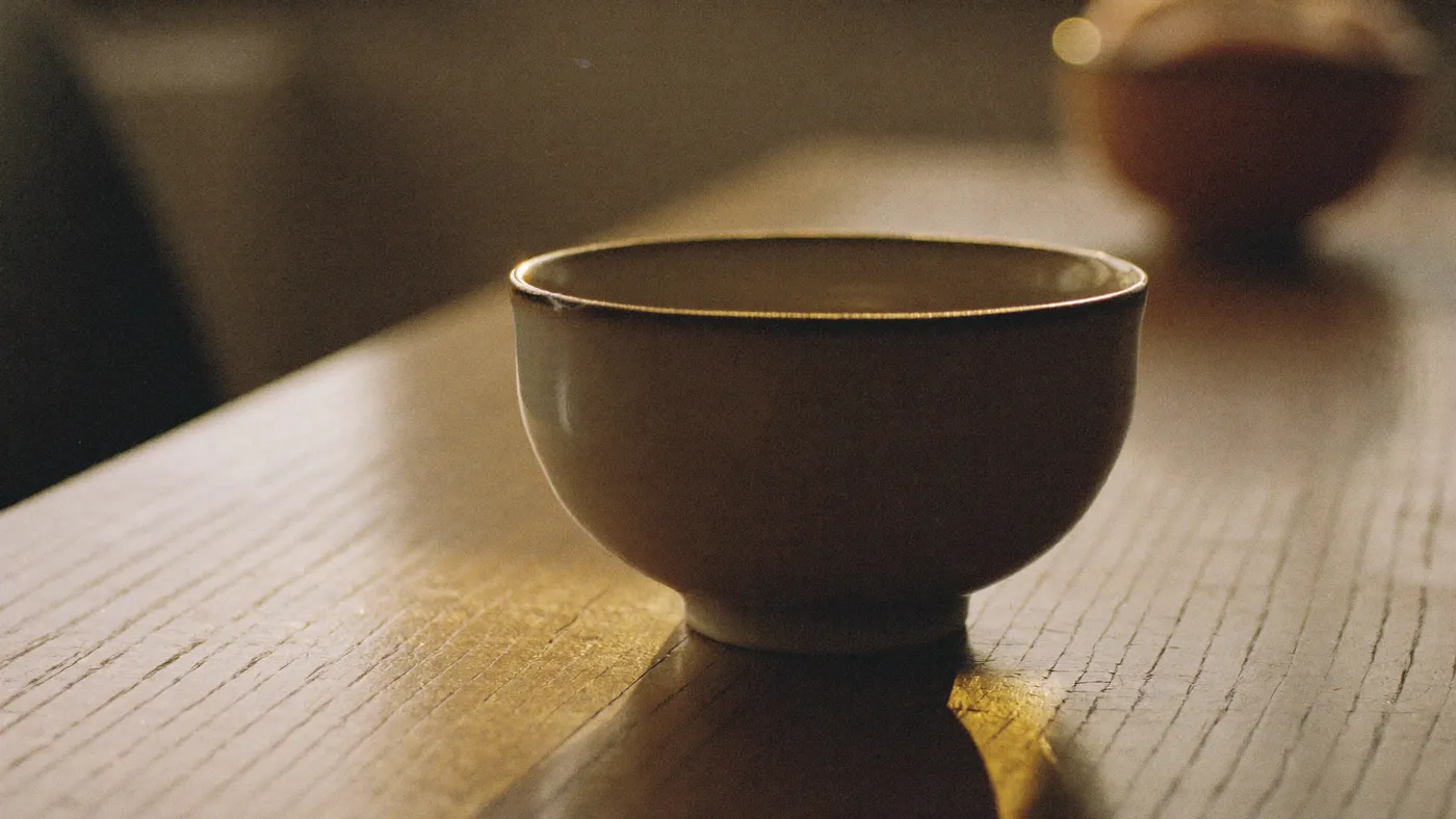 A ceramic bowl with a visible repaired crack sitting on a wooden table in soft morning light