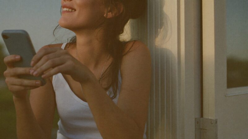Person sitting on a doorstep holding a phone with a soft blank glowing screen, about to type, warm evening light, hopeful