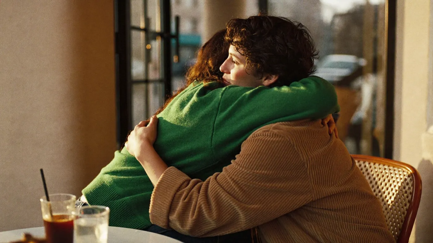 Two friends hugging at a cafe doorway at golden hour, candid and warm, seen from the side
