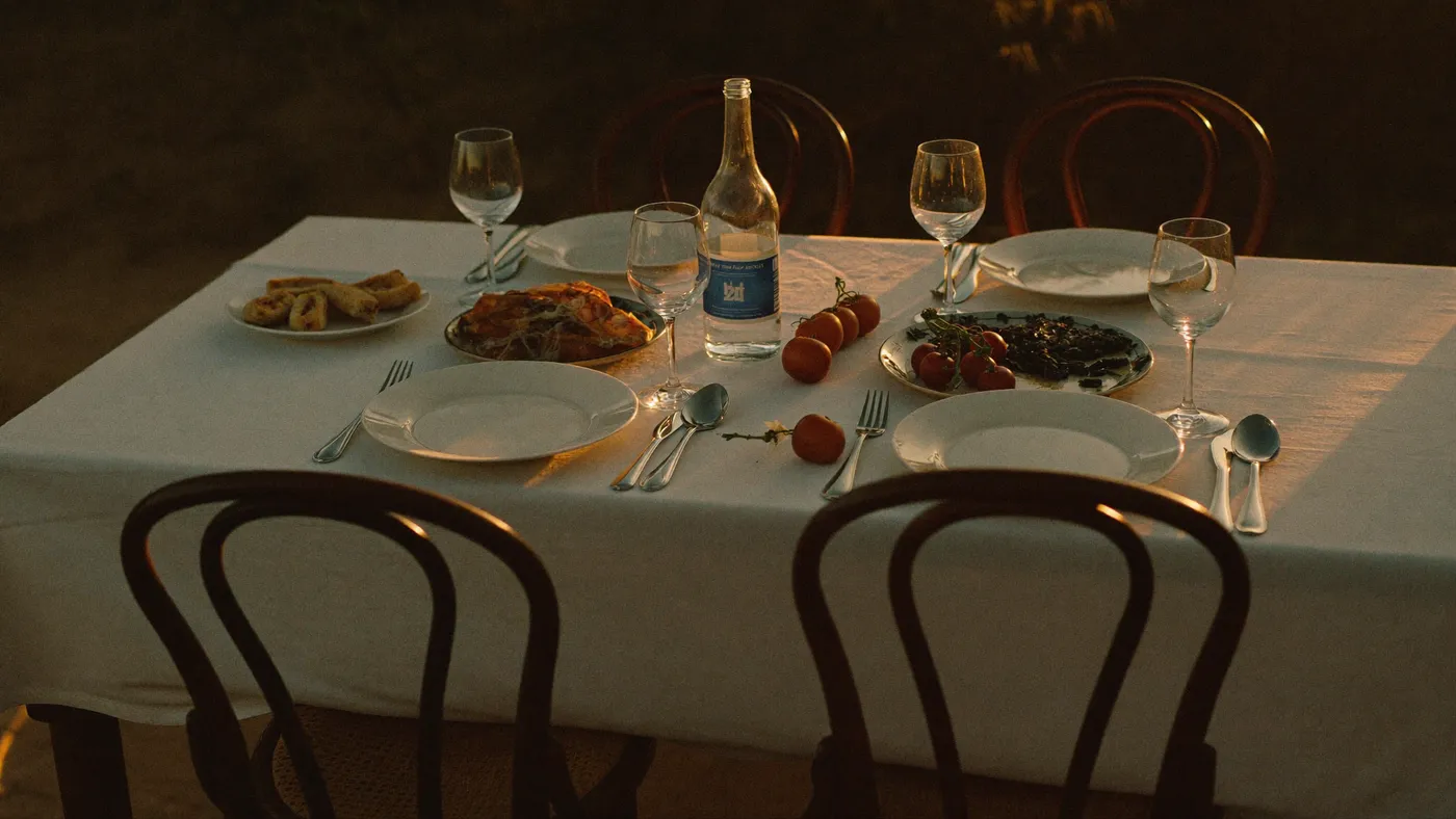 A dining table set for a family meal with empty chairs in warm evening light