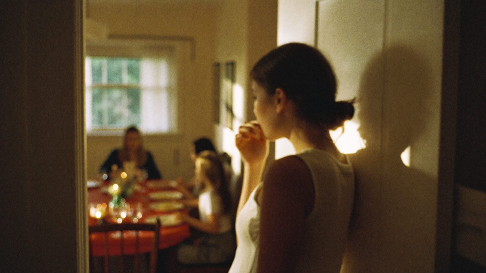 Person taking a quiet breath in a hallway outside a lively family dinner, warm light spilling from the doorway